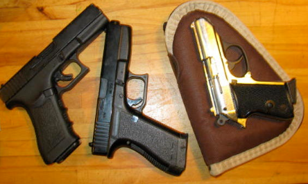 Three prop theatrical handguns — two black semi-automatics and a gold pistol in leather holster, non-firing replicas for film and TV