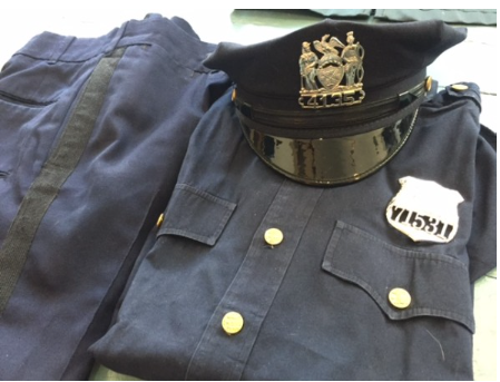 1950s NYPD police officer summer uniform — navy cap, shirt with badge number, and pants laid flat