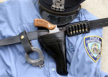 1970s NYPD big city police officer uniform — blue shirt with badge, leather belt, holster with revolver, handcuffs, and cartridge pouch