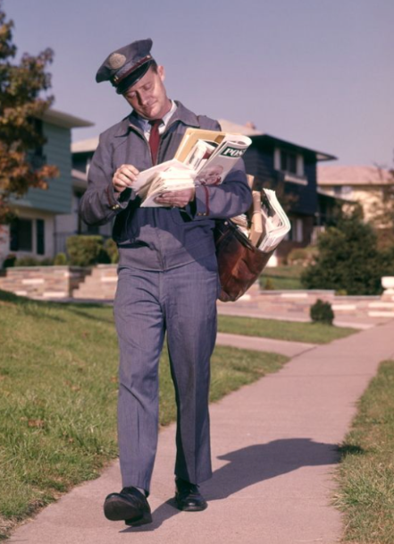 Vintage US mailman in uniform delivering mail on suburban street, 1950s