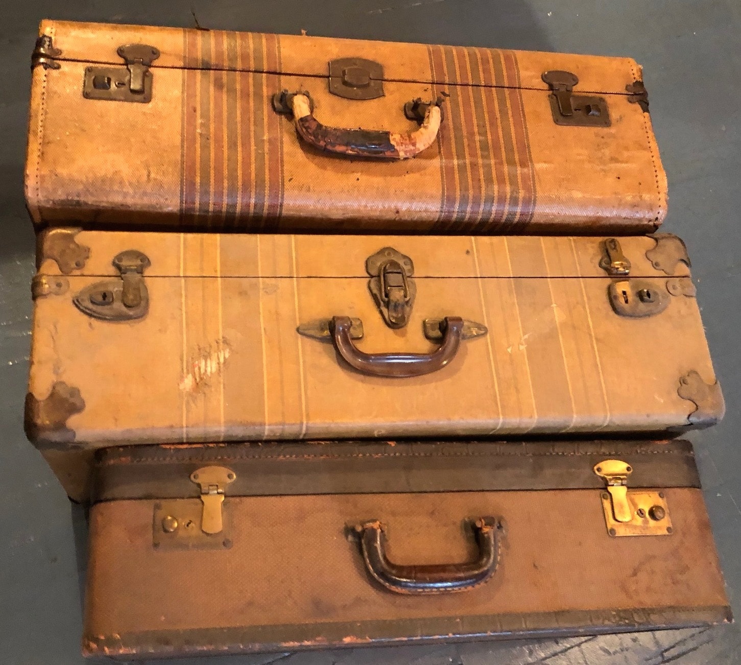 Stack of three vintage hard-shell suitcases with brass hardware and leather handles